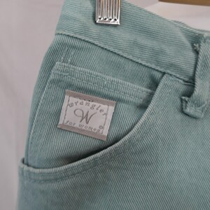 K&ouml;nnte beinhalten: Nahaufnahme einer hellt&uuml;rkisen Jeans. Die Jeans hat eine Vordertasche mit einem kleinen Etikett mit der Aufschrift "Wrangler for women". Die Jeans h&auml;ngt an einem Holzkleiderb&uuml;gel.