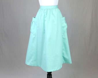 May include: A solid mint green midi skirt featuring a high waistband, a flared silhouette, and two large patch pockets on the front. The skirt has a clean, smooth finish and falls below the knee, showcasing a simple design with visible vertical seams.