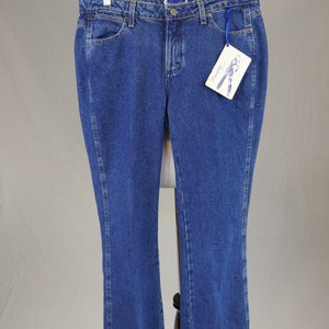 May include: Blue denim jeans with a classic five-pocket design. The jeans have a straight leg cut and a button and zipper closure. A tag with a drawing of jeans is attached to the jeans. The jeans are displayed on a mannequin.
