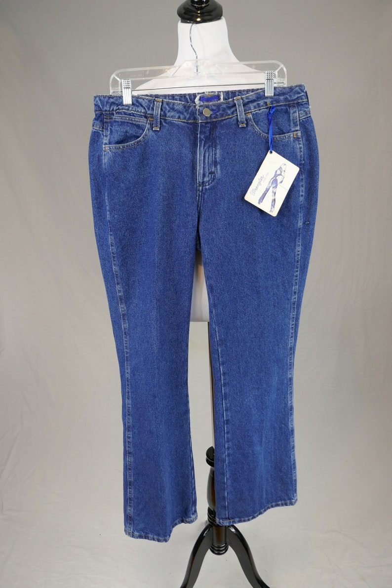 May include: Blue denim jeans with a classic five-pocket design. The jeans have a straight leg cut and a button and zipper closure. A tag with a drawing of jeans is attached to the jeans. The jeans are displayed on a mannequin.