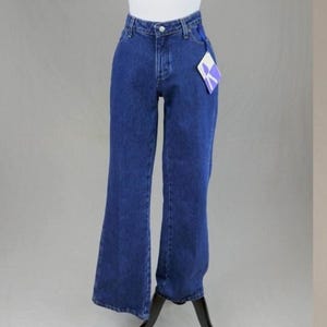 May include: Dark blue denim jeans with a high waist and flared leg. The jeans have a button and zipper closure, belt loops, and pockets. A tag is attached to the jeans. The jeans are displayed on a mannequin.
