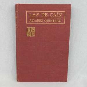 May include: A vintage, red-covered book titled "LAS DE CAÍN" by Álvarez Quintero. The title and author's name are in gold lettering within a gold rectangular frame. A gold emblem is below the title. The book has a textured cover.