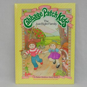 May include: A yellow book cover with a green and white Cabbage Patch Kids logo. The title is "The Just-Right Family" and the book is a Parker Brothers Story Book. The cover features an illustration of two Cabbage Patch Kids dolls walking in a forest.