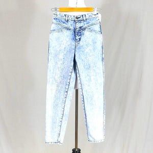 May include: High-waisted acid wash jeans in light blue with a faded, mottled effect. These jeans feature a classic five-pocket design, a button and zip fastening, and a high waist. The jeans are displayed on a mannequin.