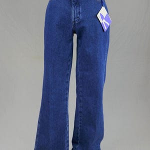 May include: Dark blue denim jeans with a flared leg design. The jeans have a classic five-pocket style, a button and zipper closure, and a tag attached to the waistband. The jeans are displayed on a mannequin.