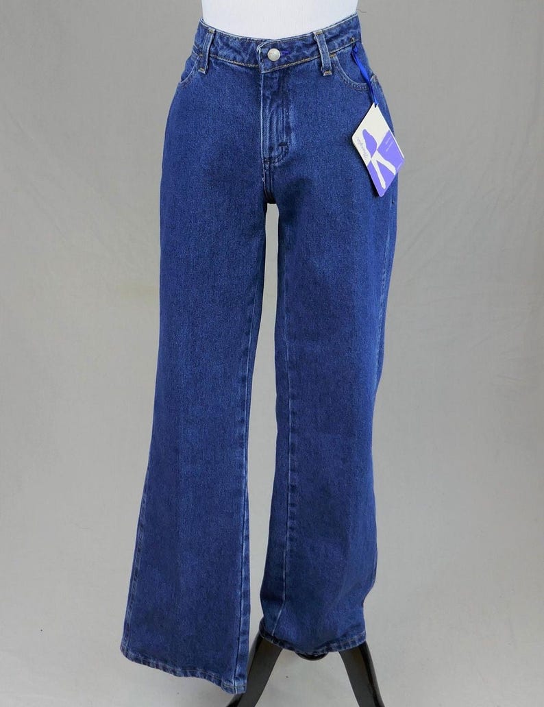 May include: Dark blue denim jeans with a flared leg design. The jeans have a classic five-pocket style, a button and zipper closure, and a tag attached to the waistband. The jeans are displayed on a mannequin.