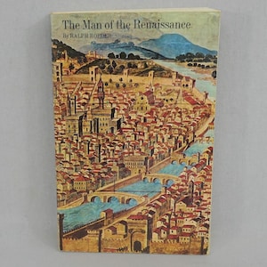 May include: A vintage book titled "The Man of the Renaissance" by Ralph Roeder. The cover features a detailed illustration of a European city with red-roofed buildings, bridges, and a river, set against a backdrop of mountains and a blue sky.