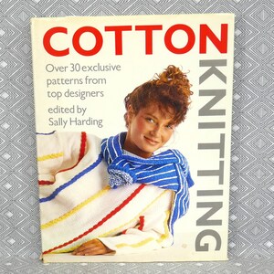 May include: A book titled "Cotton Knitting" with a white cover and red text. The cover features a woman wearing a striped white, blue, and red sweater with a blue and white striped scarf. The text on the cover reads "Over 30 exclusive patterns from top designers edited by Sally Harding."
