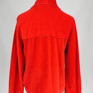 May include: A bright red corduroy jacket featuring a classic collar, long sleeves, and a horizontal back yoke seam. The garment is constructed from a textured, vertically ribbed fabric and is displayed on a mannequin to show its structure.