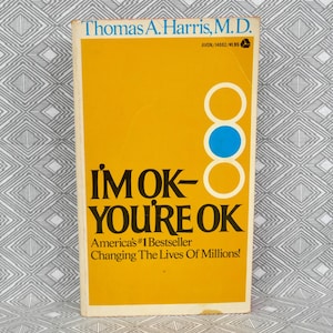 May include: A vintage paperback book titled "I'm OK - You're OK" by Thomas A. Harris, M.D. The book has a bright yellow cover with black and white text and a blue circle. The cover also states "America's #1 Bestseller".