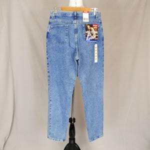 May include: Light blue denim jeans with a relaxed fit, featuring a classic five-pocket design. The jeans have a faded wash and a Wrangler label on the back pocket. The jeans are displayed on a mannequin.