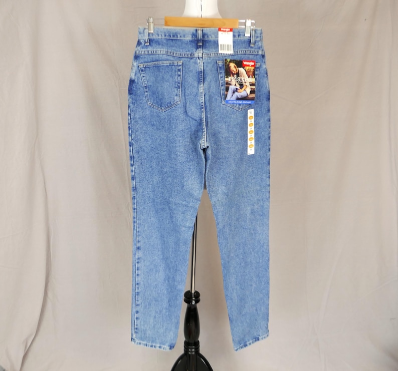 May include: Light blue denim jeans with a relaxed fit, featuring a classic five-pocket design. The jeans have a faded wash and a Wrangler label on the back pocket. The jeans are displayed on a mannequin.