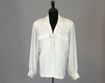 May include: A long-sleeved, off-white button-down shirt featuring a pointed collar, two chest pockets with flaps, and buttoned cuffs. The garment is made of a semi-sheer, lightweight fabric and displays vertical pleat detailing along the front.