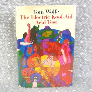May include: A hardcover book titled The Electric Kool-Aid Acid Test by Tom Wolfe. The cover features a vibrant, multi-colored illustration of a crowd of people with stylized figures in shades of red, blue, green, purple, and yellow.