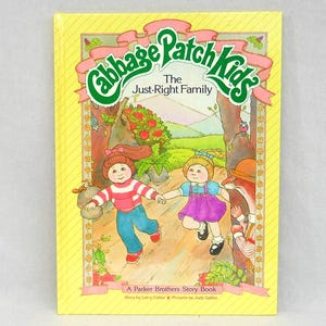 May include: A vintage children's book titled "Cabbage Patch Kids: The Just-Right Family." The cover shows an illustration of two children running through a forest scene. The book has a yellow background with a decorative border.