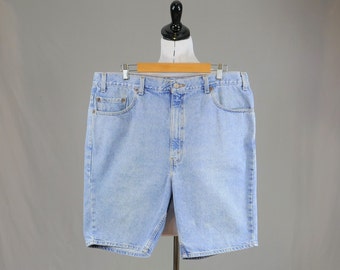 May include: Light blue denim shorts featuring a classic five-pocket design, a button and zipper fly closure, belt loops, and visible stitching along the seams. The shorts have a straight-leg cut and a medium-wash finish on the cotton fabric.