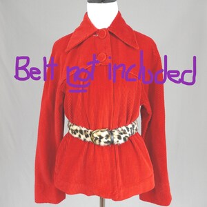May include: A bright red corduroy jacket with a pointed collar, long sleeves, and a front button closure. The jacket is displayed on a mannequin. The text "Belt not included" is written in purple across the center of the jacket.