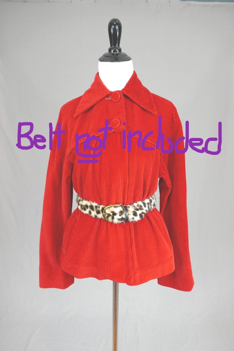 May include: A bright red corduroy jacket with a pointed collar, long sleeves, and a front button closure. The jacket is displayed on a mannequin. The text "Belt not included" is written in purple across the center of the jacket.