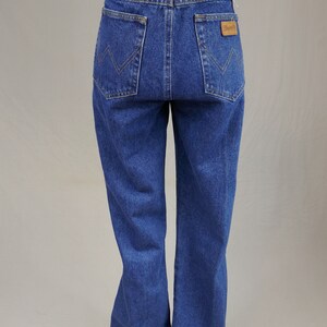 May include: Blue denim jeans with a high waist and a straight leg. The back pockets feature a distinctive stitching pattern, and a brown leather patch with the brand name is visible. The jeans are displayed on a mannequin.