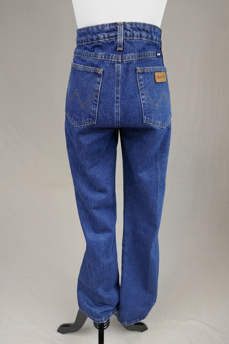 May include: Blue denim jeans with a high waist and a straight leg. The back pockets feature a distinctive stitching pattern, and a brown leather patch with the brand name is visible. The jeans are displayed on a mannequin.