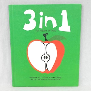 May include: A green book cover with the title "3 in 1" in white, above the text "(A Picture of God)". An illustration of a red apple with a white center is below the title. The text "WRITTEN BY JOANNE MARXHAUSEN ART BY BENJAMIN MARXHAUSEN" is at the bottom.