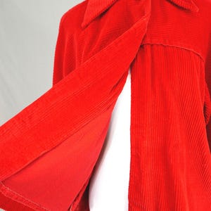 May include: A bright red corduroy jacket featuring a wide collar, a single large fabric-covered button closure at the neckline, and a flared silhouette. The jacket is made of a textured ribbed fabric and is displayed on a white mannequin form.