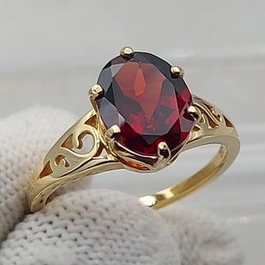 Può includere: Un anello d'oro con una pietra preziosa rossa ovale incastonata in un delicato design a filigrana.