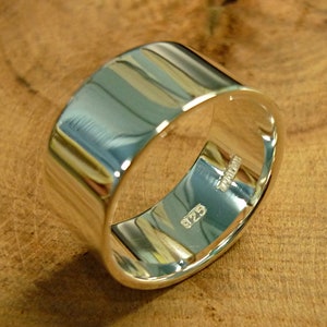 May include: A wide silver band ring with a polished finish. The inside of the band is stamped with "925".