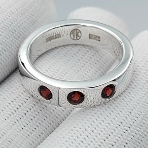 May include: A silver band ring with three red gemstones set into the band. The ring is marked "925" and "1K" on the inside.