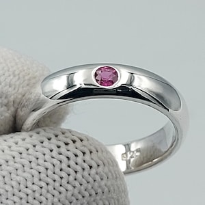 May include: A silver band ring with a single pink gemstone set in the center.