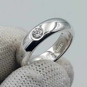May include: A silver band ring with a single round clear stone set in the centre. The ring is marked "14K" on the inside.