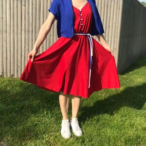 May include: A red dress with a blue and white trim, a blue cropped cardigan, and white sneakers.