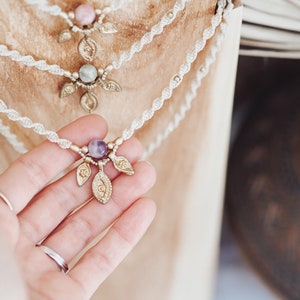 May include: A delicate white cord necklace with a purple gemstone and three gold leaf charms.