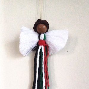 May include: A white yarn angel ornament with a brown wooden head and a red, white, green, and black yarn tassel.