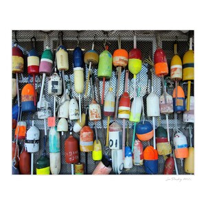 Puede incluir: Una pared con una colecci&oacute;n de adornos de madera con forma de boya, coloridos, con n&uacute;meros y letras. Las boyas cuelgan de un fondo de malla met&aacute;lica.