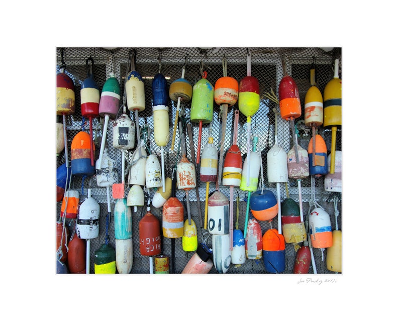 Puede incluir: Una pared con una colecci&oacute;n de adornos de madera con forma de boya, coloridos, con n&uacute;meros y letras. Las boyas cuelgan de un fondo de malla met&aacute;lica.