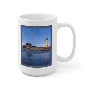 May include: White ceramic mug with a blue and white image of the Scituate Lighthouse in Massachusetts. The lighthouse is white with a green roof and a red flag on top. The image is surrounded by a blue border with the words "Scituate" and "Massachusetts" in white text.