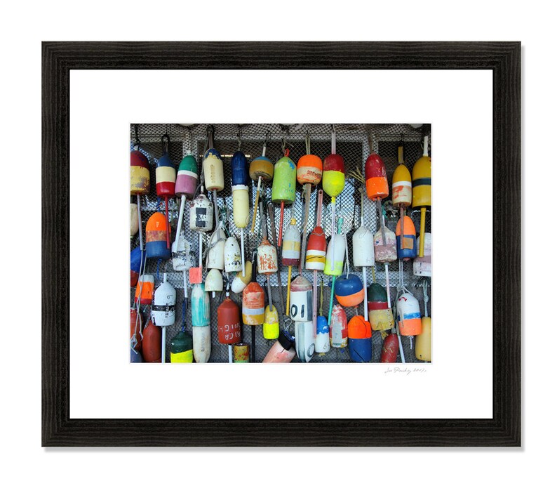 Puede incluir: Una pared con una colecci&oacute;n de boyas de madera coloridas y desgastadas con n&uacute;meros y letras pintadas. Las boyas est&aacute;n colgadas de una malla de alambre.
