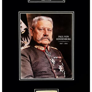 Op de afbeelding: Een ingelijst portret van Paul von Hindenburg, 1847-1934, met de persoon in een grijs militair uniform met medailles. De tekst 'Paul von Hindenburg 1847-1934' staat er twee keer op. Daaronder bevindt zich een klein rechthoekig papiertje met een handgeschreven handtekening.