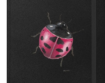 May include: Black notebook with a watercolor illustration of a ladybug. The ladybug is red with black spots and a black head. The notebook has a textured cover and an elastic band closure.
