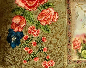 Puede incluir: Una almohada de terciopelo verde con diseños florales bordados y una imagen central de un querubín sosteniendo una cesta de flores.