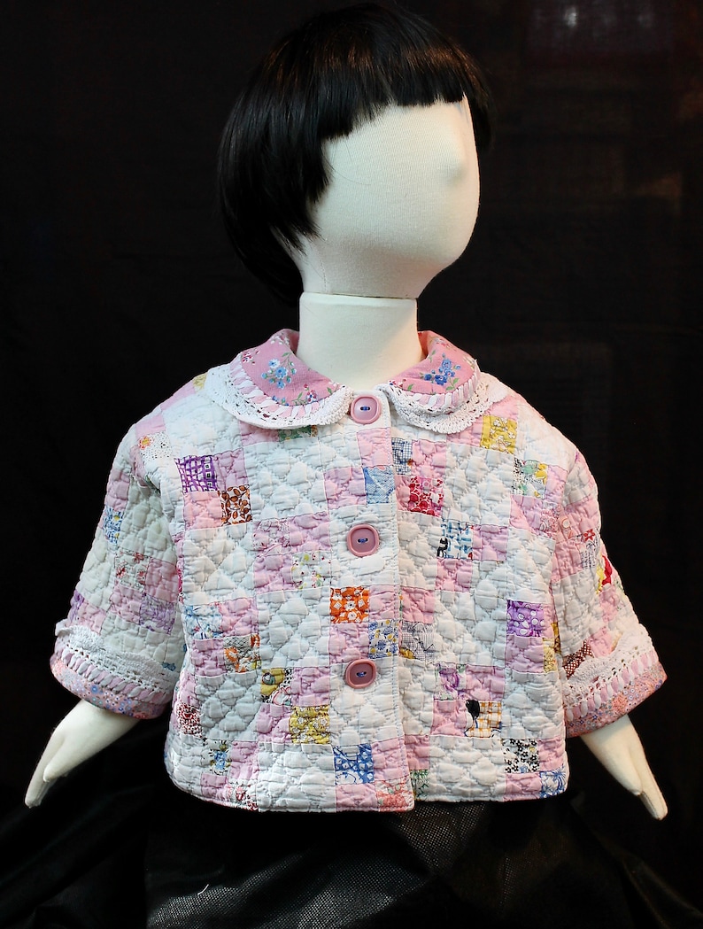 May include: A white quilted jacket with pink and floral patchwork fabric. The jacket has a white lace collar and five button fastenings.