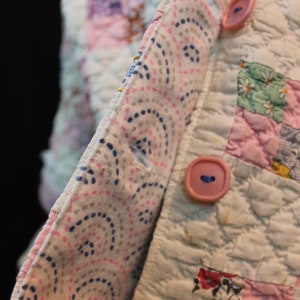 May include: A white quilted fabric with a pink and blue patterned fabric sewn to the edge. The fabric has two pink buttons.