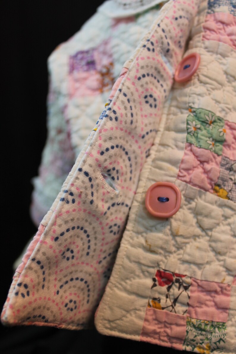 May include: A white quilted fabric with a pink and blue patterned fabric sewn to the edge. The fabric has two pink buttons.