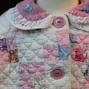 May include: A pink and white quilted jacket with a lace trim collar and two pink buttons. The jacket is made of patchwork fabric with a variety of floral patterns.