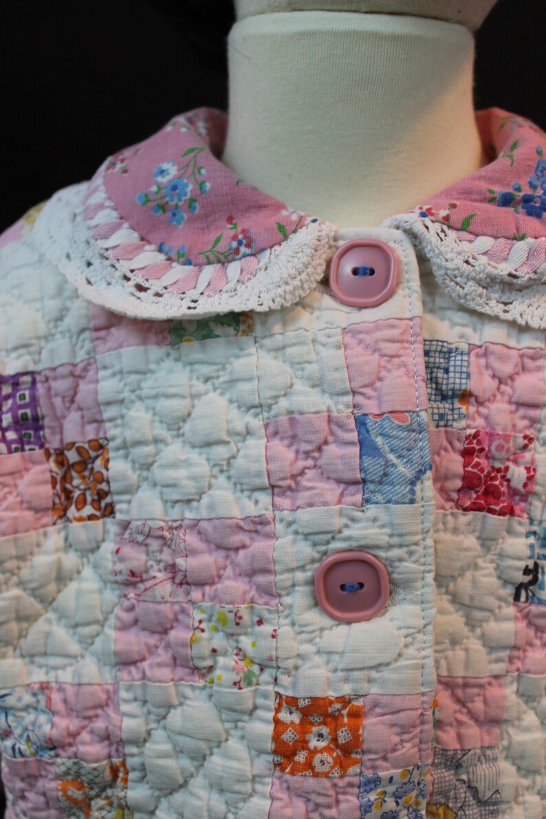 May include: A pink and white quilted jacket with a lace trim collar and two pink buttons. The jacket is made of patchwork fabric with a variety of floral patterns.