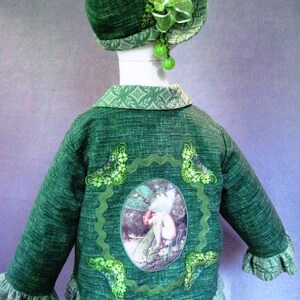 May include: Green jacket with a green and white floral design and a fairy applique. The jacket has a ruffled hem and a green hat with a white flower.