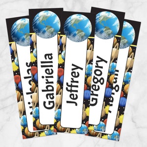 May include: Five colorful bookmarks with a space theme. Each bookmark features a black background with a white rectangle for a name. The bookmarks have a pattern of planets, stars, and a yellow sun. The names on the bookmarks are Nicholas, Gabriella, Jeffrey, Gregory, and Jason.