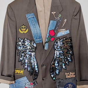 May include: A brown blazer decorated with denim patches, sequined wings, and various embroidered patches including text that reads Expensive, God Bless the Hustle, and Give Me My Roses While I'm Here, plus a circular patch stating Be the Best Version of Yourself.