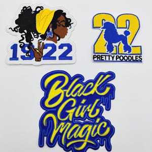 May include: Three embroidered patches with a white background. One patch features a black woman with a yellow head wrap and the numbers "1922". Another patch has the number "22" with a blue poodle and the words "Pretty Poodles". The third patch says "Black Girl Magic".
